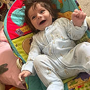 Henry is registered to the contest to win money with this photo: animal_print, baby, baby_seat, candid, child, clothing, colorful, cute, face, hair, happy, indoor, infant, joyful, living_room, pajamas, playful, smiling, soft_toys, young_child