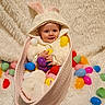 baby, bunny_costume, basket, plastic_eggs, easter, fluffy_blanket, smiling, cute, child, indoor, soft_texture, colorful, holiday, festive, toy, portrait, cozy, playful, holiday_theme, happy