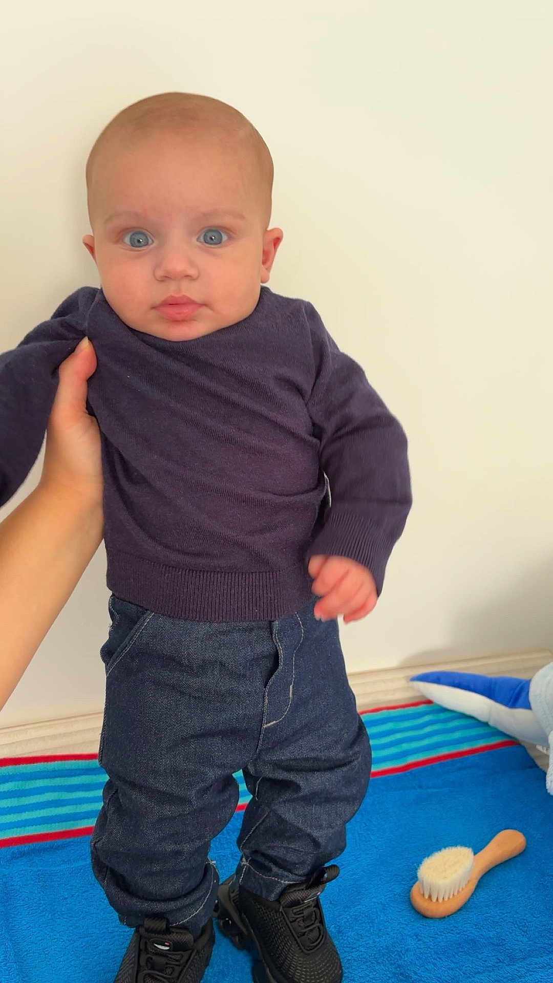 Bastien a rejoint le concours — aidez-le/la à gagner de superbes lots ! baby, child, blue_eyes, purple_sweater, denim_pants, black_shoes, hand, striped_blanket, brush, indoor, person, standing, floor, toy, curious, cute, portrait, infant, clothing, soft_lighting