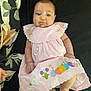 baby, infant, pink_dress, easter_theme, bunny, colorful_eggs, blanket, floral_pattern, lying_down, cute, chubby_cheeks, hand, foot, soft_fabric, indoors, portrait, child, smiling, face, person