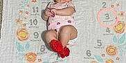 Lily joined the competition — help win amazing prizes! baby, infant, child, milestone_blanket, red_headband, red_booties, pink_onesie, carpet, floor, flower_pattern, months, laying_down, cute, portrait, indoors, adorable, clothing, person, young_child, baby_girl