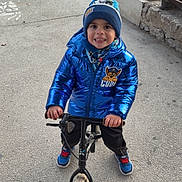Edzio participe au concours pour gagner de l'argent avec cette photo : balance_bike, beanie, bench, blue_jacket, child, concrete, cute, happy, hat, hoodie, metal_posts, outdoor, park, pavement, playing, portrait, smiling, sneakers, toy_bike, winter_clothing