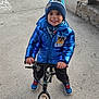 balance_bike, beanie, bench, blue_jacket, child, concrete, cute, happy, hat, hoodie, metal_posts, outdoor, park, pavement, playing, portrait, smiling, sneakers, toy_bike, winter_clothing
