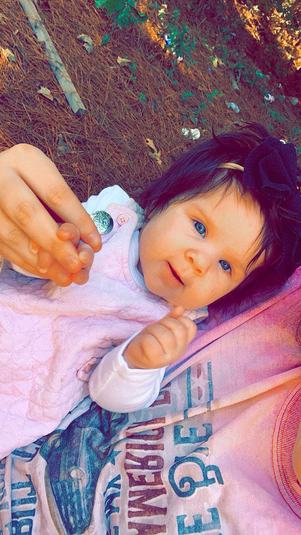 Charleigh Kate is registered to the contest to win money with this photo: baby, child, blue_eyes, bow, hand_holding, pink_clothing, outdoor, grass, leaves, person, cute, portrait, infant, young_child, happy, smiling, headband, face, skin, closeup