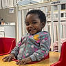 Daqariah joined the competition — help win amazing prizes! toddler, child, smile, high_chair, hoodie, floral_pattern, table, indoor, furniture, face, person, cute, happy, hair, wooden_table, baby, hand, seat, room, background