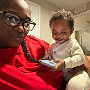 Daqariah joined the competition — help win amazing prizes! adult, baby, child, glasses, indoor, living_room, phone, smile, red_shirt, braid, curly_hair, white_clothing, holding, person, home, casual, joy, family, portrait, happy