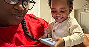 Daqariah joined the competition — help win amazing prizes! adult, baby, child, glasses, indoor, living_room, phone, smile, red_shirt, braid, curly_hair, white_clothing, holding, person, home, casual, joy, family, portrait, happy