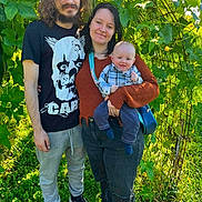 Zayden is registered to the contest to win money with this photo: baby, child, family, parents, infant, smiling, portrait, outdoor, garden, foliage, plants, greenery, sunlight, standing, holding, toddler, shirt, clothing, nature, family_portrait