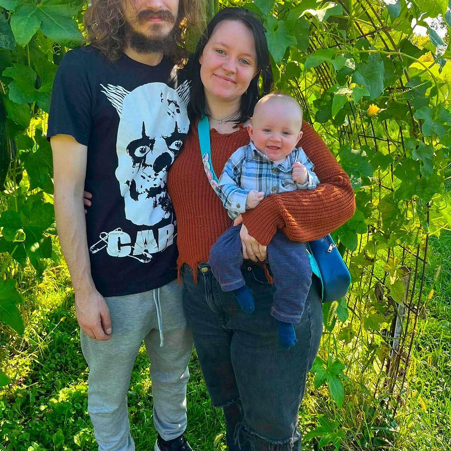 Zayden is registered to the contest to win money with this photo: baby, child, family, parents, infant, smiling, portrait, outdoor, garden, foliage, plants, greenery, sunlight, standing, holding, toddler, shirt, clothing, nature, family_portrait
