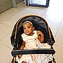 Anaya participe au concours pour gagner de l'argent avec cette photo : baby, child, stroller, dress, headband, indoor, floor, tile, open_door, footwear, lace, person, infant, seated, curious, light, window, black_skin, cute, portrait