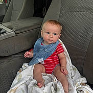 Tucker is registered to the contest to win money with this photo: baby, car_seat, blanket, blue_bib, red_onesie, child, infant, interior, vehicle, seat, fabric, sunset, window, curious, clothing, person, sitting, young_child, casual, indoors