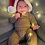Oliver is registered to the contest to win money with this photo: baby, santa_hat, knitted_outfit, fairy_lights, smiling, couch, cozy, holiday, festive, indoors, cute, child, portrait, warm_lighting, happy, infant, playful, soft_texture, celebration, relaxing