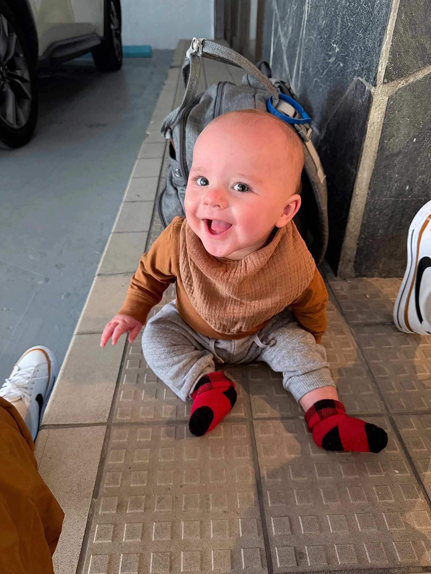 Oliver is registered to the contest to win money with this photo: baby, child, smiling, sitting, floor, tiles, socks, clothing, backpack, happy, person, indoor, footwear, casual, cute, portrait, head, face, human, expression