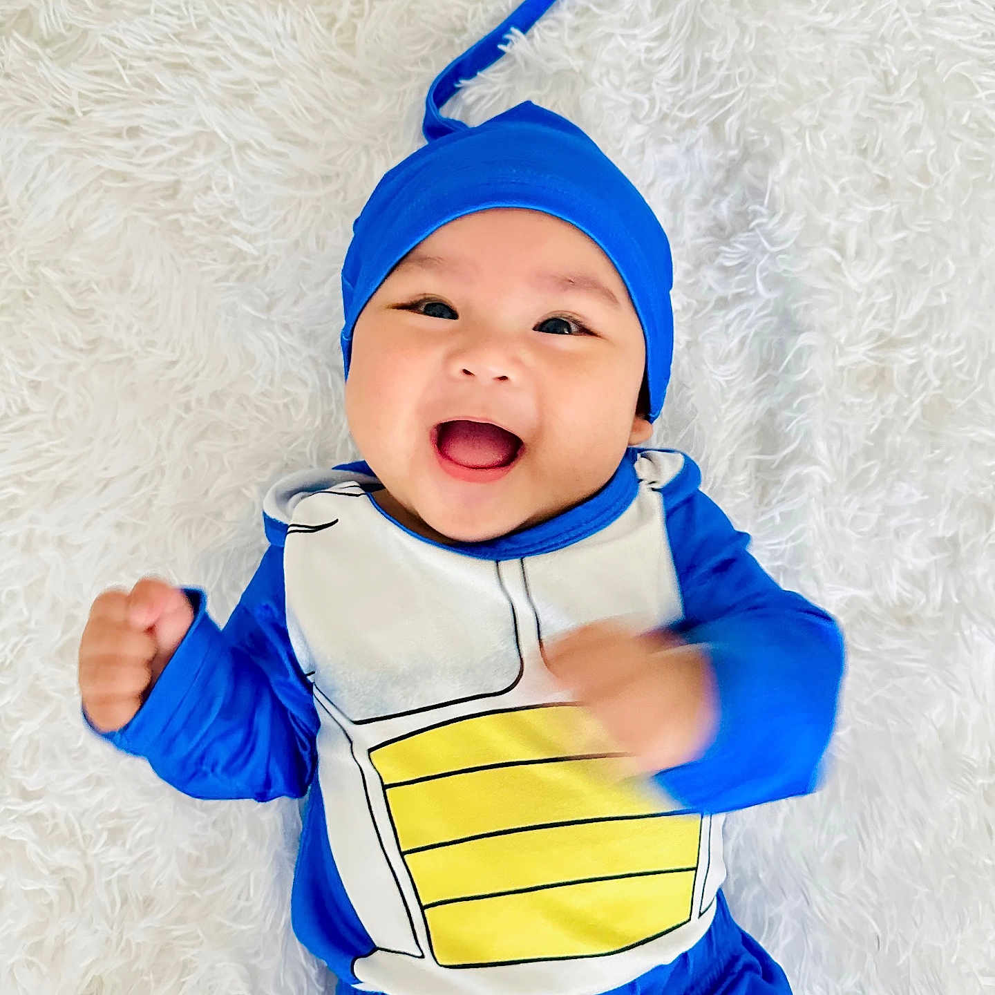 Andy is registered to the contest to win money with this photo: baby, smiling, blue_costume, yellow, happy, infant, lying_down, fluffy_background, cute, child, headwear, motion_blur, portrait, young_child, playful, costume, indoors, bright_colors, fun, expression