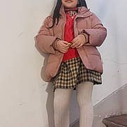 Lucie a rejoint le concours — aidez-le/la à gagner de superbes lots ! child, girl, jacket, sweater, skirt, tights, sneakers, stairs, indoor, wall, standing, holding, long_hair, casual_clothing, plaid, white_wall, wooden_stairs, portrait, smiling, fashion