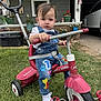 toddler, child, tricycle, radio_flyer, outdoor, grass, overalls, white_shoes, handlebars, porch, house, american_flag, plants, window, door, concrete, sidewalk, red, playful, curious