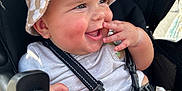 Anakin is registered to the contest to win money with this photo: baby, child, smiling, hat, bucket_hat, checkered, stroller, seatbelt, happy, cute, infant, clothing, hand, face, cheeks, fingers, outdoor, daylight, closeup, person