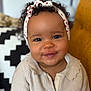 baby, child, smiling, headband, curly_hair, sweater, indoor, portrait, cute, cozy, face, person, seated, furniture, cushion, pattern, red_hearts, knitwear, expression, happy