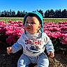 baby, child, blue_hat, sweatshirt, disney, stitch, flowers, pink_flowers, field, outdoor, nature, greenery, sky, sunlight, young_child, sitting, cute, portrait, daylight, grass