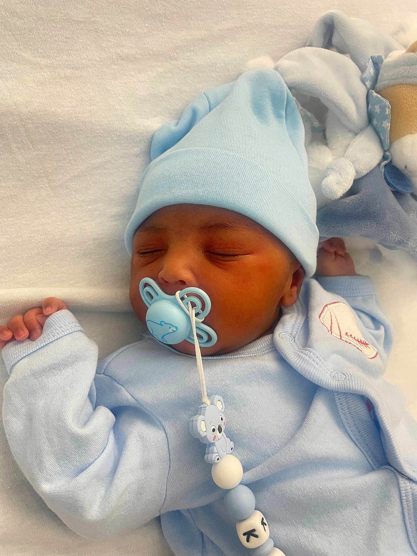 Jayden a rejoint le concours — aidez-le/la à gagner de superbes lots ! baby, newborn, sleeping, pacifier, blue_clothing, hat, soft_toy, blanket, bed, infant, cute, peaceful, indoors, closeup, child, rest, comfort, face, hand, toddler