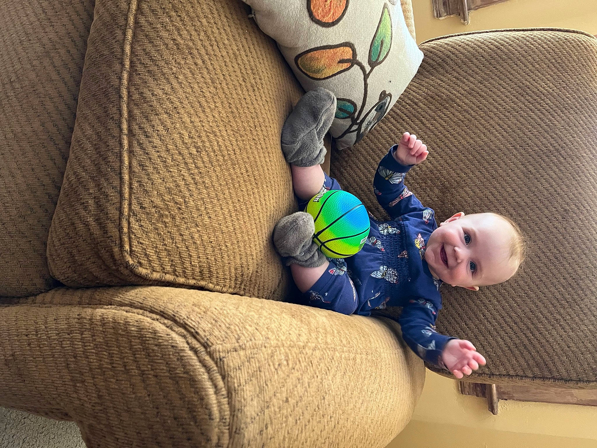 Zia is registered to the contest to win money with this photo: baby, baby_toddler_clothing, ball, comfort, couch, elbow, finger, flooring, hand, human_body, human_leg, joy, knee, leg, person, sitting, sneakers, sock, textile, thigh