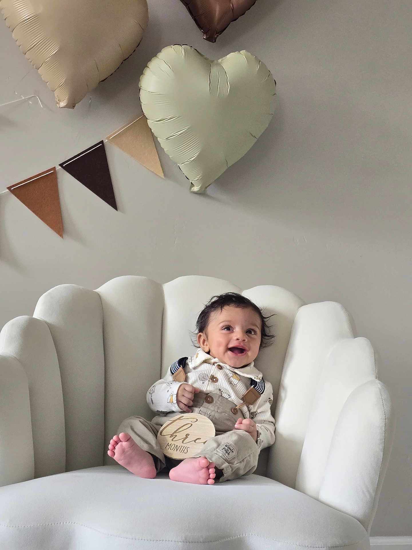 Uday joined the competition — help win amazing prizes! baby, infant, chair, white_chair, heart_balloon, balloon, banner, smiling, happy, clothing, overalls, feet, indoors, celebration, decor, person, portrait, cute, three_months, toddler