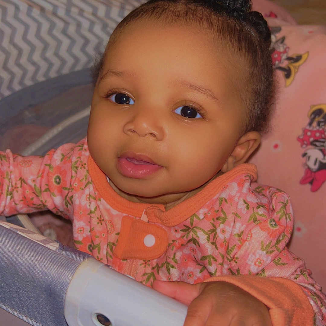 Niamani-Marie is registered to the contest to win money with this photo: baby, blanket, braids, child, clothing, cute, face, floral_pattern, hand, indoor, infant, mickey_mouse, nursery, person, pink, playpen, portrait, smiling, soft_lighting, young_child