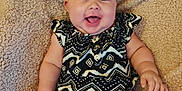 Parker is registered to the contest to win money with this photo: baby, child, smiling, headband, flower, patterned_clothing, black_and_white, shorts, sitting, blanket, beige, happy, cute, infant, chubby_arms, indoors, portrait, face, person, cozy