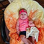 Parker is registered to the contest to win money with this photo: baby, infant, pink_headband, pink_top, blanket, fluffy_cushion, orange_cushion, cream_cushion, baby_seat, wooden_floor, cardboard_box, indoor, person, child, cute, soft_texture, relaxed, calm, small_feet, human