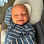 baby, infant, face, smile, blue_clothing, striped_clothing, onesie, cushion, gray_cushion, relaxing, portrait, indoor, child, young, human, comfort, soft, resting, cute, happy
