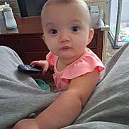 Autumn is registered to the contest to win money with this photo: arm, baby, bottle, carpet, child, couch, curious, face, fireplace, furniture, home, indoor, infant, living_room, person, pink_clothing, remote_control, sitting, table, toy