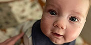 Phoenix is registered to the contest to win money with this photo: baby, bed, bib, blanket, child, clothing, curious, cute, dinosaur_pattern, eyes, face, hair, hand, indoor, infant, person, portrait, skin, soft_focus, young