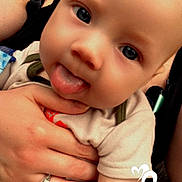 Phoenix is registered to the contest to win money with this photo: baby, tongue_out, hand, ring, adult, close_up, face, eyes, skin, clothing, holding, expression, cute, infant, person, portrait, love, heart_graphic, casual, outdoor