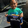 Noëlan participe au concours pour gagner de l'argent avec cette photo : child, smiling, indoor, shirt, holding, braided_hair, green_tshirt, spiderman, marble_floor, flag, name_print, portrait, happy, casual_clothing, young_child, person, bright_lighting, shadow, black_floor, closeup