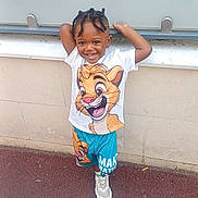 Noëlan participe au concours pour gagner de l'argent avec cette photo : child, smiling, braids, cartoon_clothing, shorts, tshirt, sneakers, outdoor, wall, pavement, happy, standing, casual, playful, portrait, person, young, fashion, cute, daylight