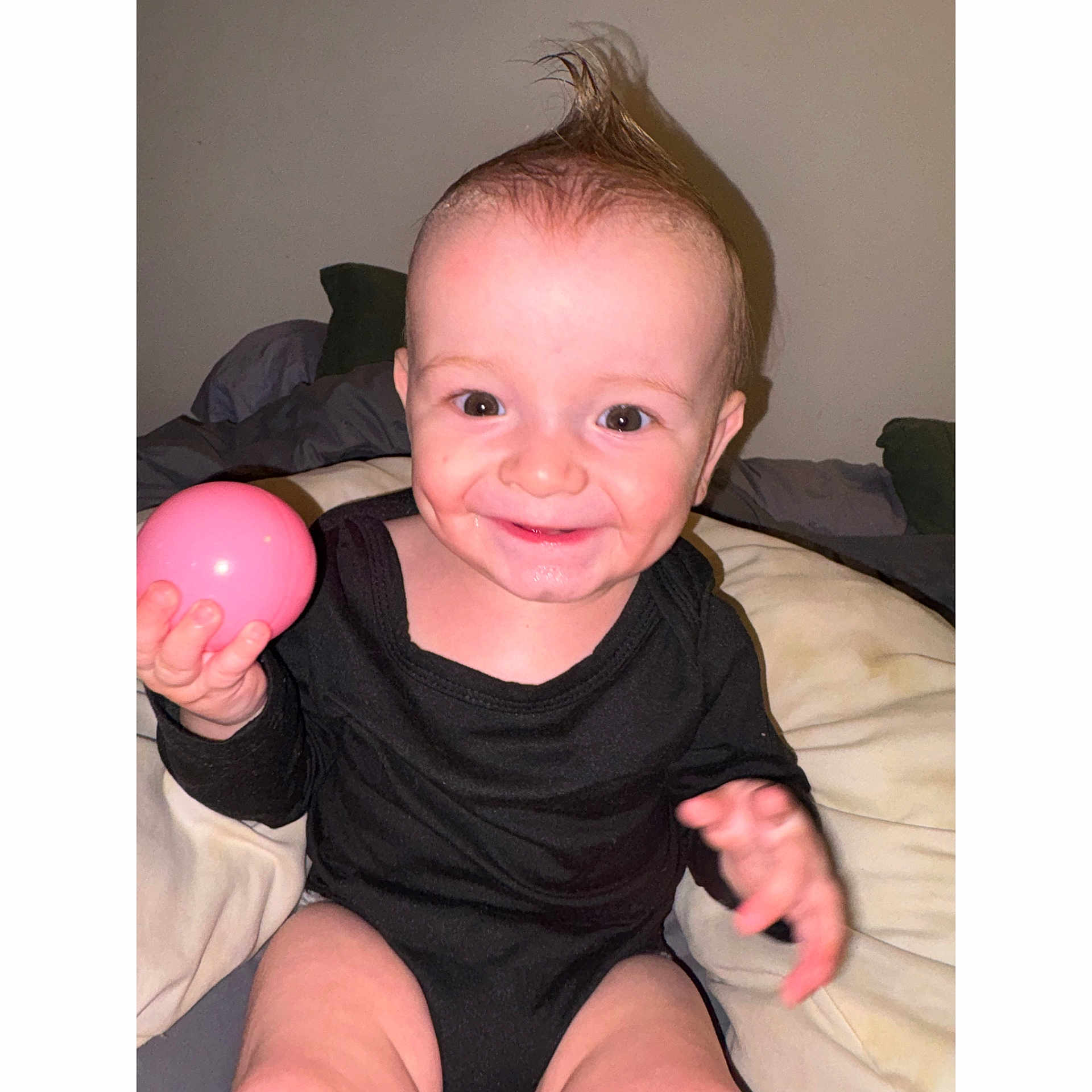 Lyam a rejoint le concours — aidez-le/la à gagner de superbes lots ! baby, child, smiling, happy, face, hand, ball, black_clothing, mohawk, indoor, bed, blanket, person, cute, infant, playful, skin, expression, young, sitting