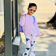 Evelyn joined the competition — help win amazing prizes! child, girl, sunglasses, purple_cardigan, unicorn_design, heart_pants, backpack, sidewalk, outdoor, peace_sign, casual_clothing, shoes, sunlight, shadow, urban, portrait, fashion, cute, standing, playful