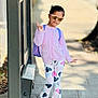 child, girl, sunglasses, purple_cardigan, unicorn_design, heart_pants, backpack, sidewalk, outdoor, peace_sign, casual_clothing, shoes, sunlight, shadow, urban, portrait, fashion, cute, standing, playful