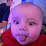 John Lee is registered to the contest to win money with this photo: baby, tongue_out, close_up, red_shirt, wide_eyes, person, adult, pillow, sleeping, bed, blanket, blue_tone, indoor, face, expression, cute, child, infant, home, relaxed