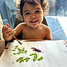 art, brush, child, colorful, creative, curly_hair, expression, finger_paint, happy, indoor, messy, painting, paper, person, playful, portrait, smiling, table, toddler, young_child