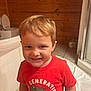 child, boy, smile, red_tshirt, dinosaur_graphic, indoor, bathroom, tile_floor, bathtub, wooden_wall, short_hair, cute, happy, young, person, casual_clothing, portrait, standing, light, home