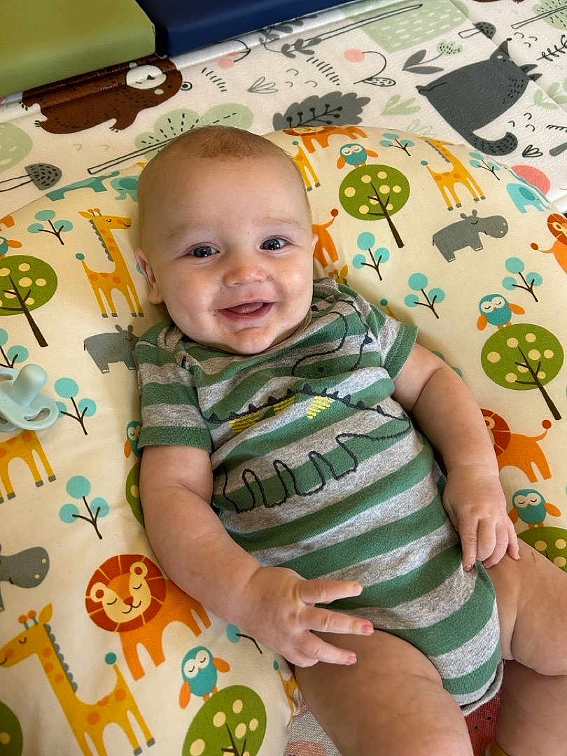 Chase is registered to the contest to win money with this photo: baby, smiling, infant, onesie, green_stripes, animal_print, cushion, colorful, playmat, giraffe, lion, owl, hippopotamus, hand, face, cute, happy, indoor, child, portrait