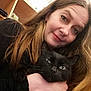 woman, cat, black_cat, indoor, selfie, long_hair, hand, shelf, bottle, face, pet, holding, portrait, casual, expression, home, animal, cute, feline, closeup