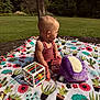Stormi joined the competition — help win amazing prizes! baby, child, outdoor, blanket, toy, plush, cube_toy, grass, nature, sunlight, greenery, flower_pattern, cactus_pattern, sitting, infant, cute, daytime, playtime, colorful, clothing