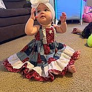 Stormi is registered to the contest to win money with this photo: baby, bow, carpet, child, colorful_clothing, couch, curious, cute, dress, family, floor, girl, headband, indoor, infant, living_room, patchwork, person, playpen, sitting