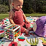 baby, child, outdoor, grass, tree, blanket, toy, plastic_toy, plush_toy, pink_clothing, romper, sunlight, nature, cute, sitting, infant, face, expression, colorful, playtime