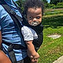 Rowan is registered to the contest to win money with this photo: adult, baby_carrier, barefoot, blue_shirt, casual_clothing, child, close_up, curly_hair, daylight, green_grass, holding, nature, outdoor, pacifier, person, shadow, side_view, sunny, toddler, trees