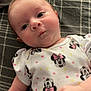 baby, infant, child, onesie, mickey_mouse, minnie_mouse, polka_dots, blanket, plaid, face, chubby_cheeks, curious, lying_down, cute, skin, hand, expression, indoors, soft_lighting, clothing