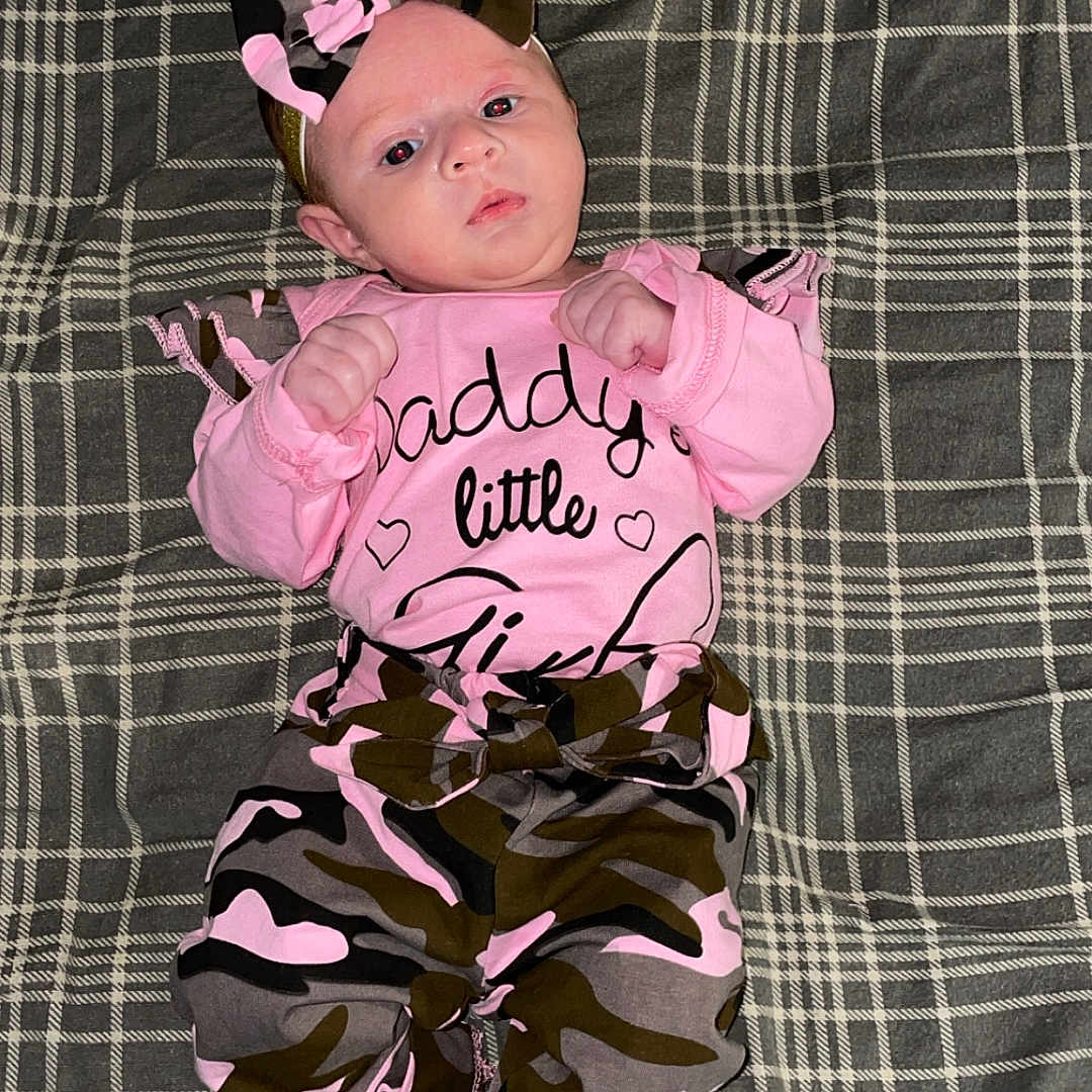 Oaklee joined the competition — help win amazing prizes! apparel, baby, blanket, bow, camouflage, child, clothing, cute, fabric, face, feet, hands, indoors, infant, lying_down, newborn, person, pink, plaid, portrait
