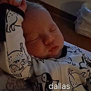 Dallas is registered to the contest to win money with this photo: newborn, baby, sleeping, infant, portrait, onesie, animal_print, clothing, indoors, bed, blanket, peaceful, face, closed_eyes, nose, mouth, head, cozy, text_overlay, dallas